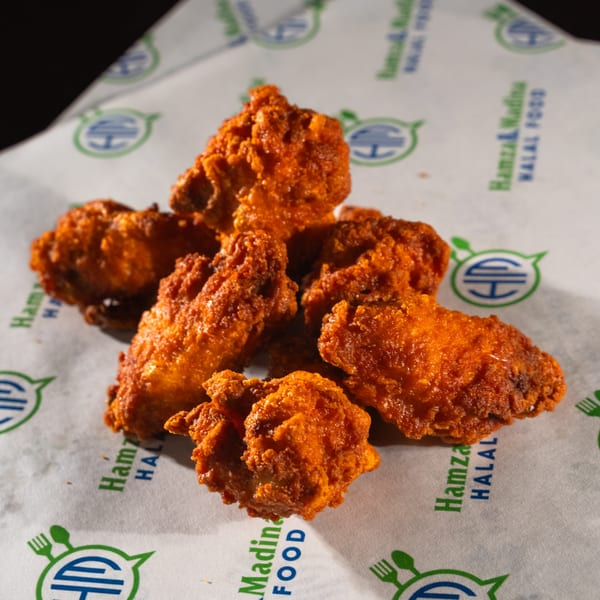 Six crispy, orange-red Hamza & Madina Halal chicken wings on branded white paper.