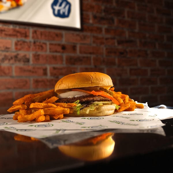 A Hamza & Madina Halal Food burger with fries on branded paper, against a brick wall.
