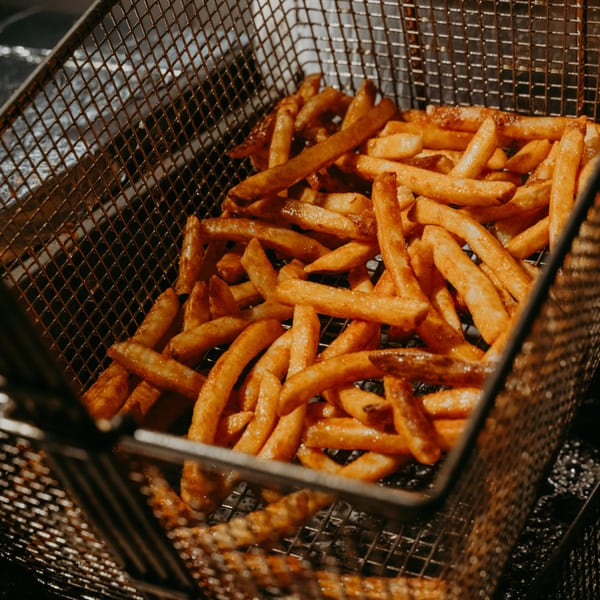 Golden-brown french fries cooking in a metal fryer basket at Hamza & Madina Halal Food.