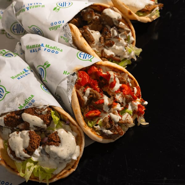 Three Hamza & Madina Halal Food wraps, one falafel, one chicken, and one mixed, on a dark surface.