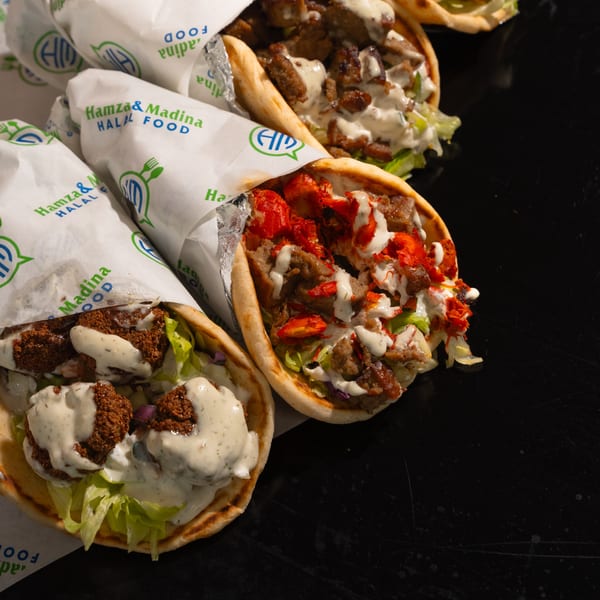 Three Hamza & Madina Halal Food wraps, one falafel and two meat, with white sauce on a dark surface.