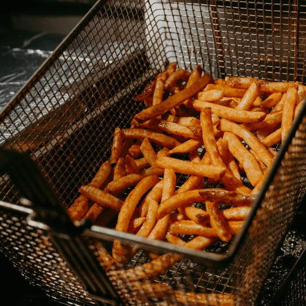 Golden-brown french fries in a metal fryer basket, ready to be served at Hamza & Madina Halal Food.