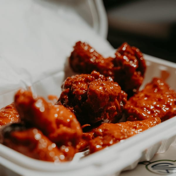 Close-up of Hamza & Madina Halal Food's saucy red chicken wings in a white takeout container.