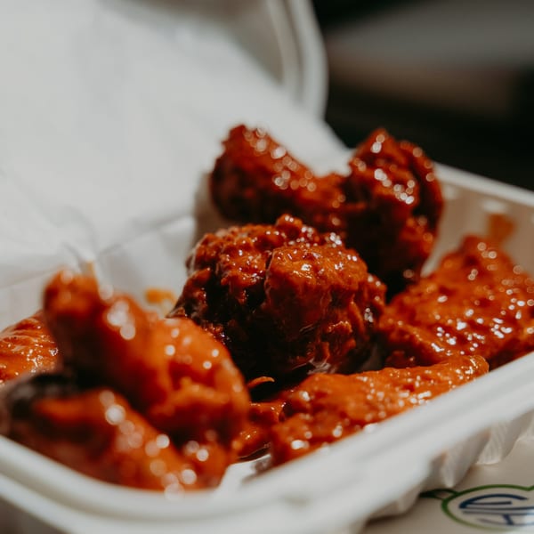 Close-up of several saucy, red-glazed chicken wings in a white takeout container.