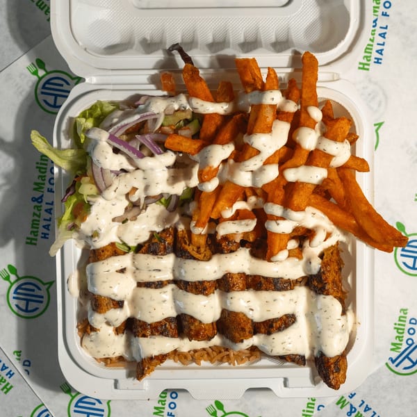 Halal food platter with chicken, rice, sweet potato fries, salad, and white sauce in a takeout container.