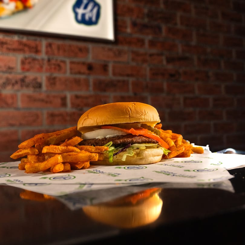 A Hamza & Madina Halal Food burger with fries on branded paper against a brick wall.